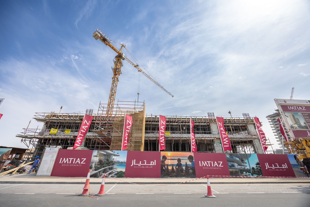 Beach Walk Iii By Imtiaz A construction site featuring scaffolding, a crane, and banners for Imtiaz Developments under a blue sky.